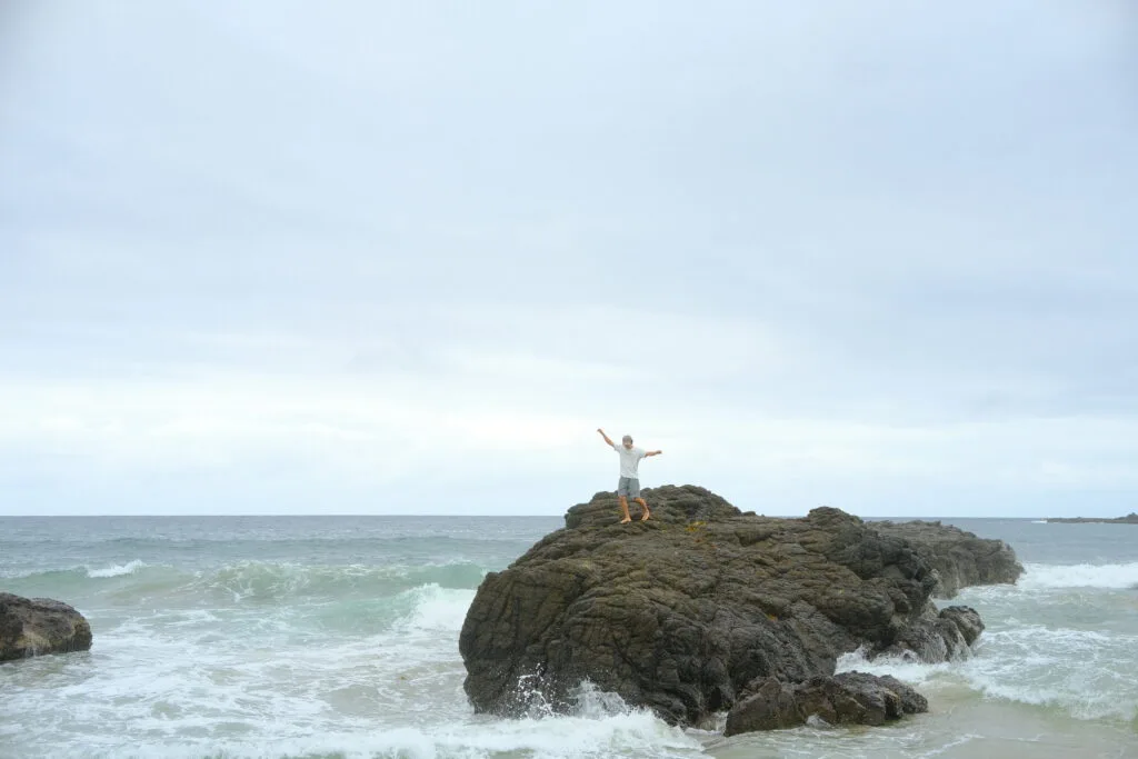 A young man balancing on the rocks in the sea.