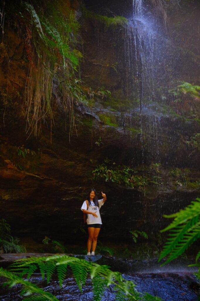 Girl giving a thumbs up under a small waterfall