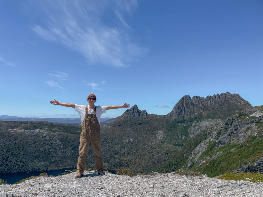 Me, arms stretched wide on top of a mountain in front of Cradle Mountain