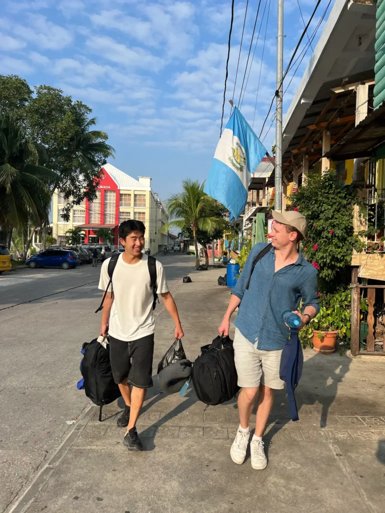 Two guys smiling and holding bags walking on the road in Flores Guatemala
