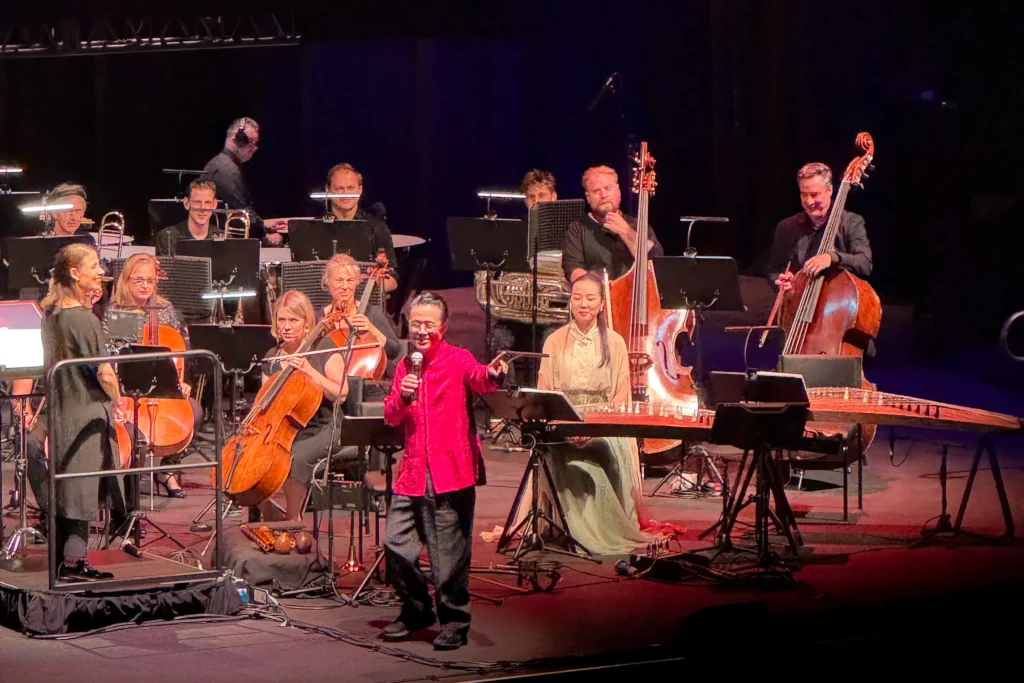 Man in read pointing and standing in front of orchestra