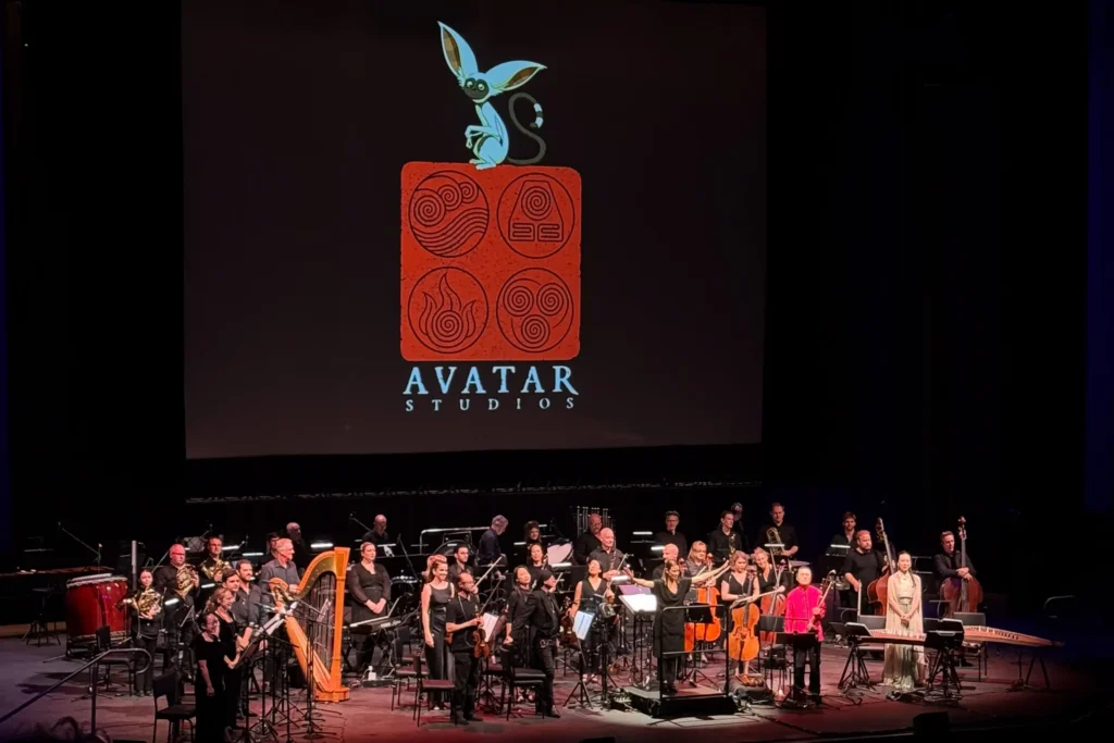 Orchestra standing in front of screen with the Avatar studios logo