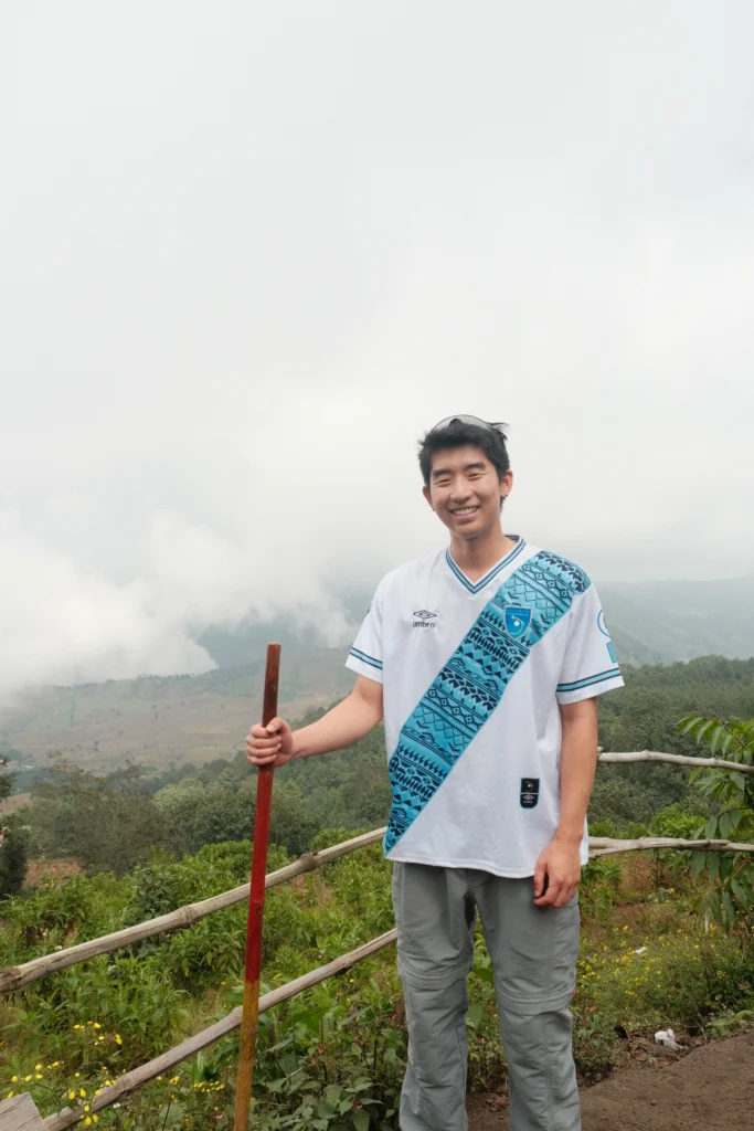 Me smiling holding a wooden walking stick, wearing a T-shirt