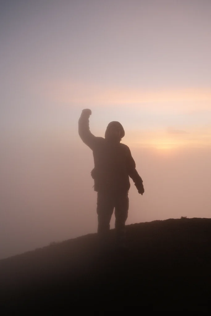 Me with my hand up on top of the summit in a jacket.