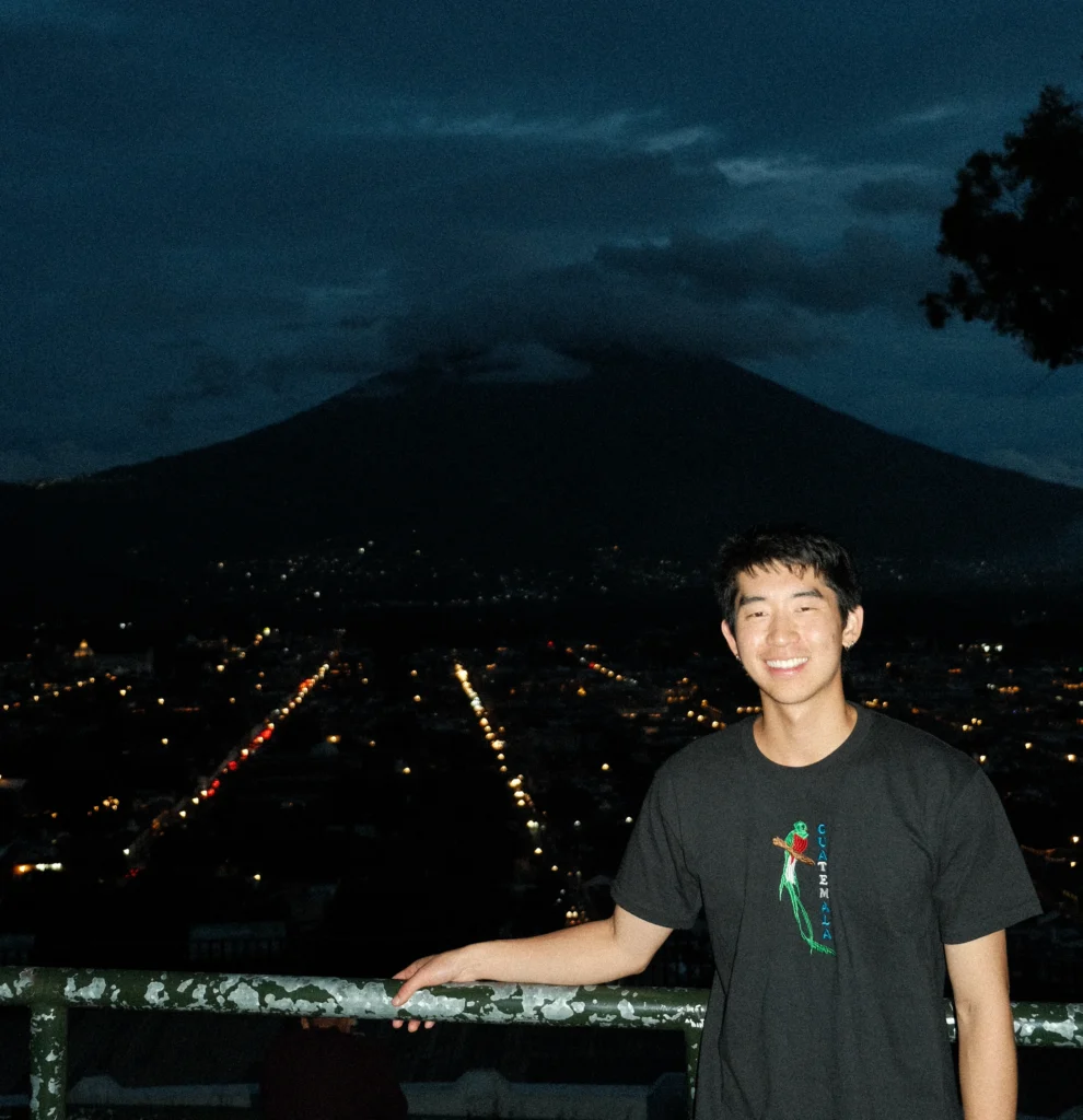 Me smiling holding onto a green railing in front of a mountain in Antigua
