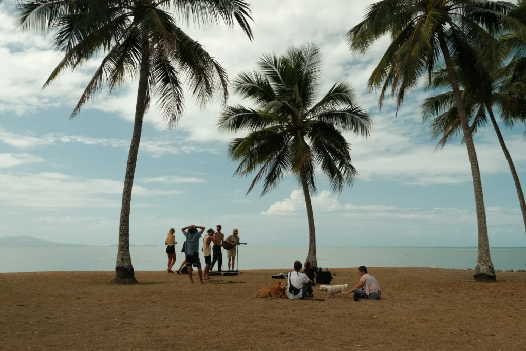 people singing and relaxing underneath palm trees by the water in Port Douglas