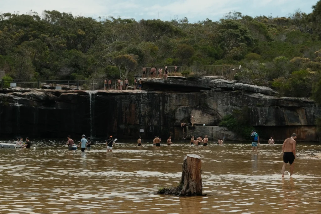A crowd of people line up on top of the waterfall ready to jump into the lagoon